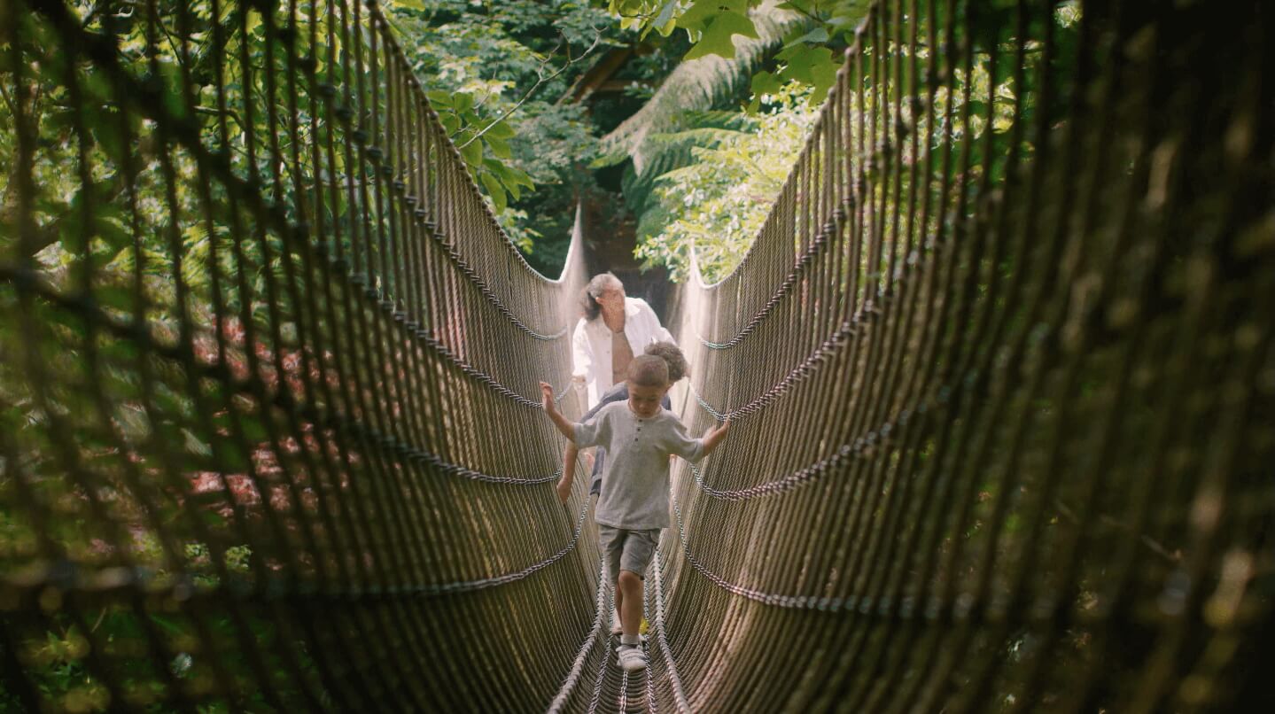 A photo of a model family crossing the rope bridge at Heligan Gardens during their Summer Brand Campaign.