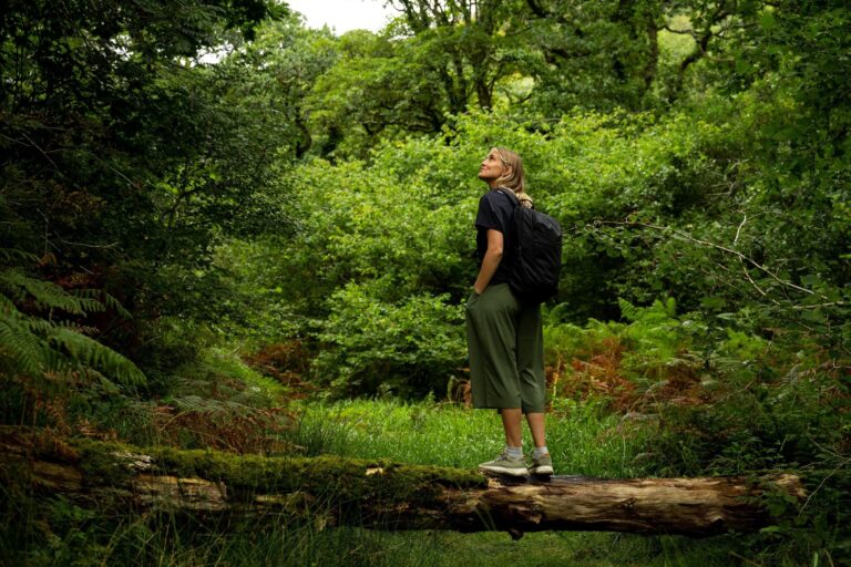 An image of sustainability influencer, Sophie Hellyer, in Kathmandu clothing standing on a log in a forest.