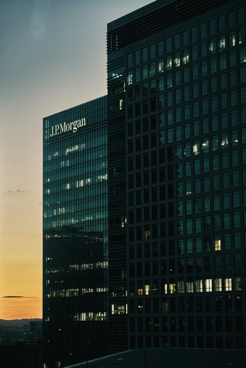 A night time shot of the outside of a JP Morgan office. The sun is rising behind the building.