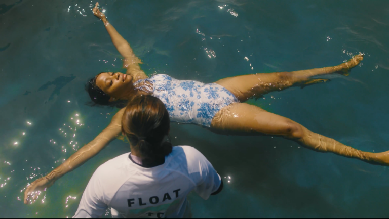 An image of a woman floating in the Bude tide pool with a member of the RNLI next to her.