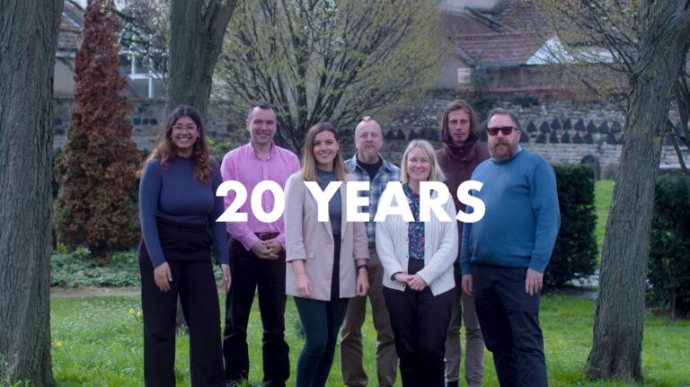 An image of the GWCU team posing for a group shot for their corporate video production. "20 Years" is written on the image in front of them.