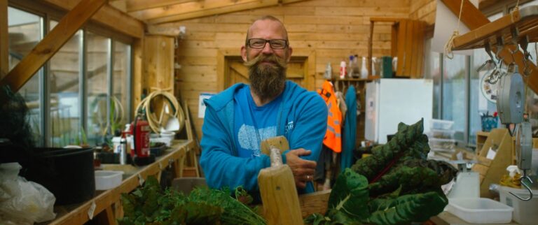 An image of a smiling male gardener from Newquay Orchard holding a basket of vegetables.