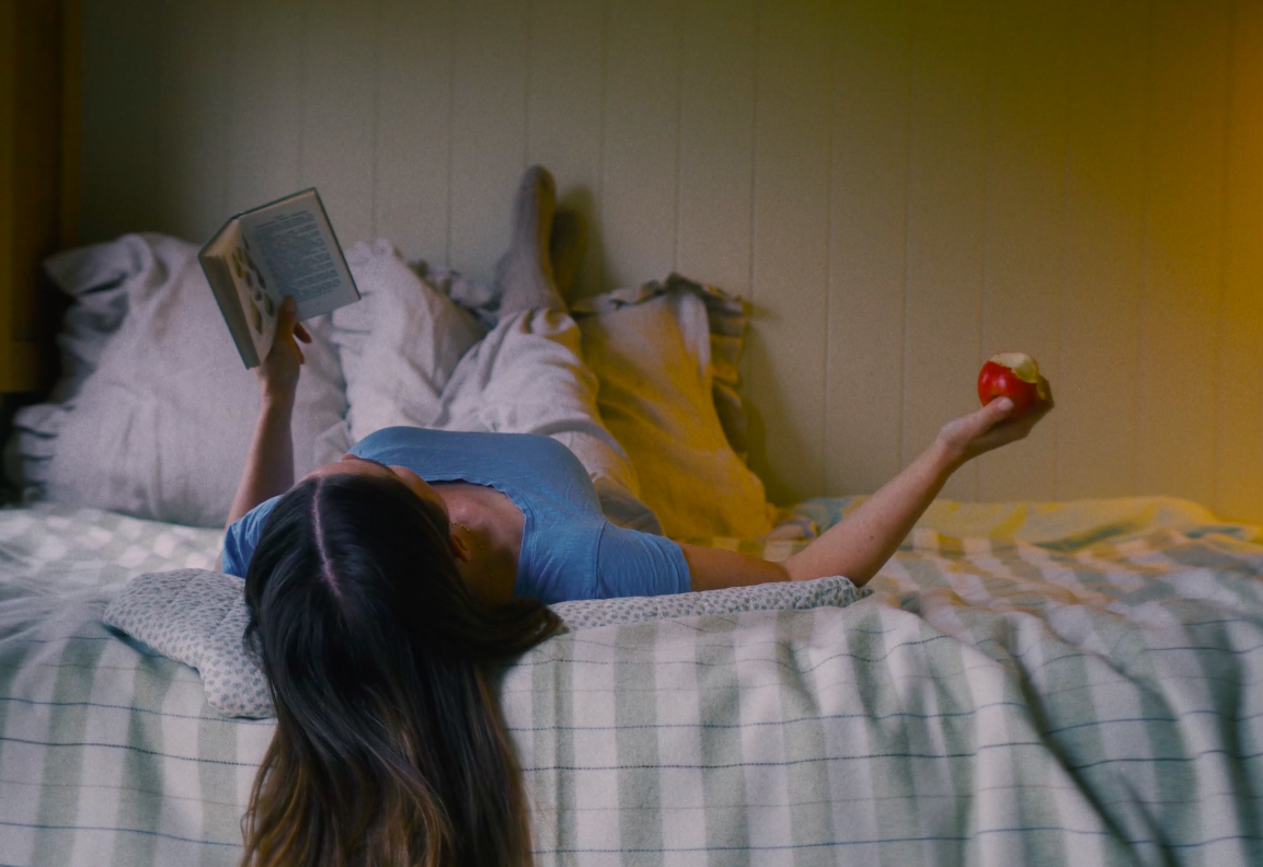 A woman reading a book in a Plankbridge Hut. She's wearing a blue t shirt and has long brown hair.