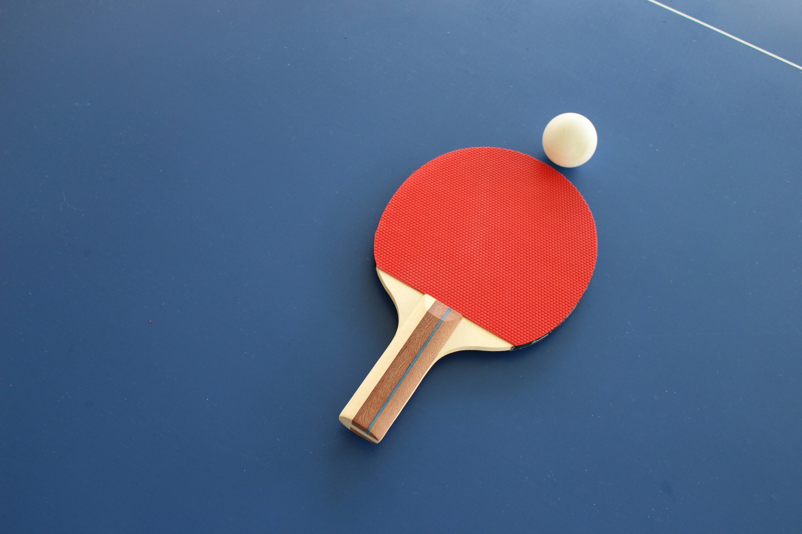 A picture of a paddle racket and ball on the floor.