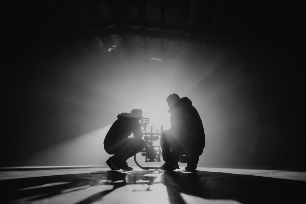 Two crew members crouched by a camera in strong backlight