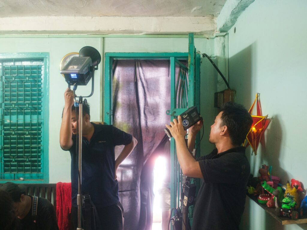 Two crew members rigging a light and a camera in a small room