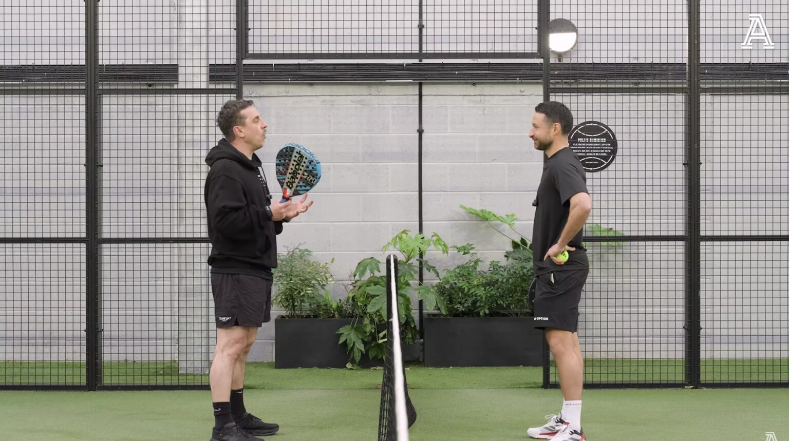 Gary Neville and David Ornstein face each other across the net on a covered padel court